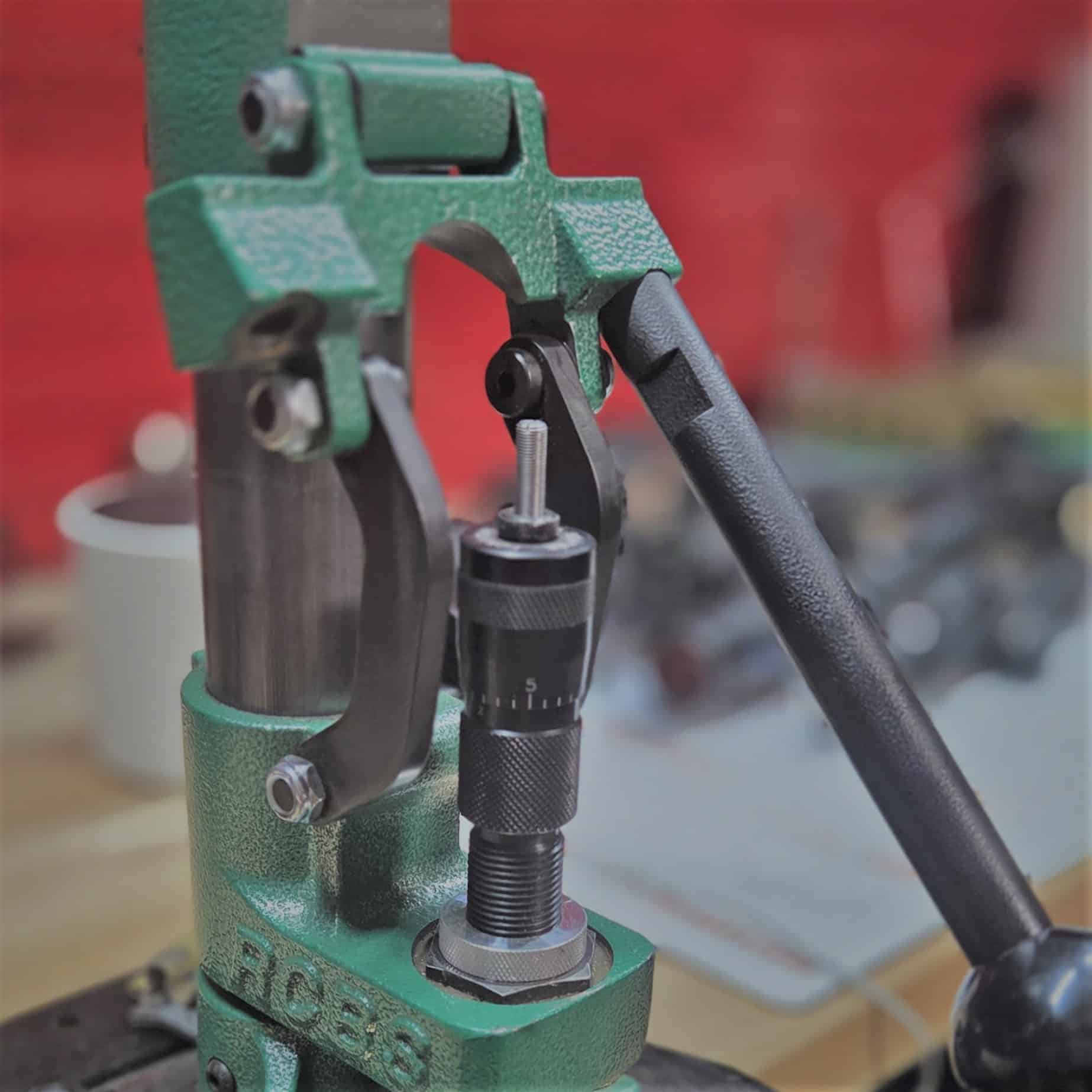 Green RCBS reloading press with handle and precision gauge in workshop setting.